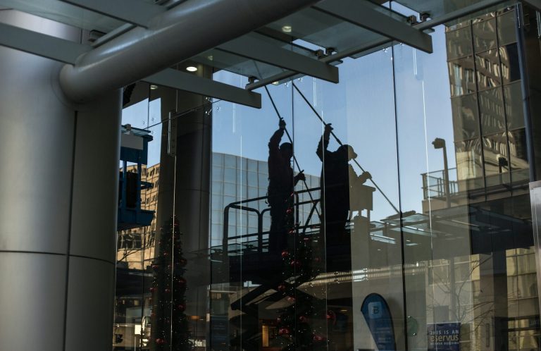 Clean Police Fensterreinigung Zwei Reinigungskräfte putzen eine Glasfassade mit einem Gerüst im Hintergrund.
