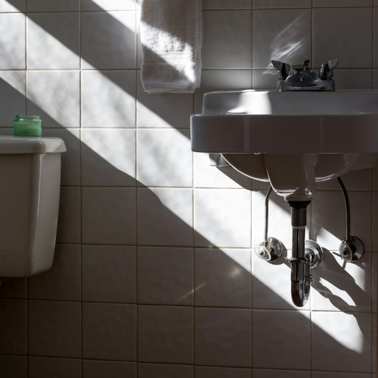 Clean Police Badreinigung Heller Badezimmerbereich mit Waschbecken und Toilette, Schatten fallen über die Fliesen.